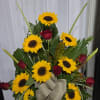 Sunflowers, red roses, assorted greenery, decorative palm leaves, and a fabric bow