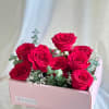 A pink rectangular box filled with red roses and fresh eucalyptus. 

Flower