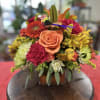This charming vase overflows with a vibrant seasonal mix of roses, marigold