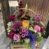 An assortment of Purple Flowers arranged in a basket around a Candle