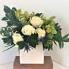 A combination of white and green flowers in a white ceramic cube