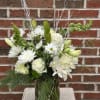 A sympathy floral design, classic white with seasonal flowers and greens. The