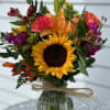 Sunflowers, Orange Lily, orange roses carnations, magenta stock
alstro and faux leaves arranged