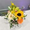 With a bold sunflower at its heart, this lively arrangement blends creamy