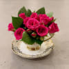Teacup with saucer filled with greenery and spray roses. 