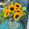 Sunflowers arranged with seasonal greenery .