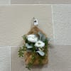 A brown wall hanger filled with artificial ranunculus and greenery. 