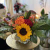 Roses, lilies, and sunflowers, nestled seasonal greens, accented with Autumn branches. A