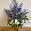 A tall one sided table arrangement of blue delphinium and white roses