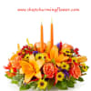 A vibrant fall centerpiece featuring two tall, orange candles surrounded by an