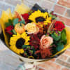 The arrangement bursts with seasonal blooms in shades of burnt orange, golden