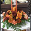 A FALL CENTERPIECE WITH ORANGE LILLIES, MIXED MUMS, ROSES, MIXED GREENS AND