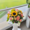 A vibrant arrangement featuring sunflowers, pink roses, peach roses, and green foliage