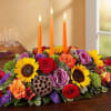 All-around centerpiece arrangement with autumn-colored roses, sunflowers, red daisy poms, orange Asiatic