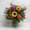 A bright mix of sunflowers, orange roses, and purple blooms arranged in