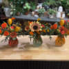 Three small mixed color bud vases with seasonal autumn blooms are the