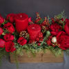 Red flowers and candles with Christmas berries, greens, pinecones and ornaments in