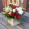 A rustic wooden box is filled with seasonal greens and flowers. Flower