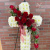 White cross adorned with red roses and greenery 