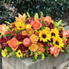 A warm, vibrant fall centerpiece bursting with golden sunflowers, orange roses, burgundy
