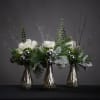 A trio of silver mercury glass budvases fist white spray roses, a