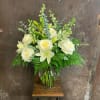 A vase of white blooms with roses, lilies and assorted greens.