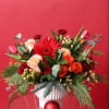 This vibrant winter arrangement combines rich reds, warm peaches, and lively oranges