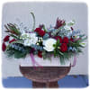 This classic holiday arrangement includes winter greens, stock, roses and bows.