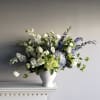 Footed compote vase overflowing with hydrangea, roses, ranunculus and other blooms.