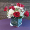 A glass cube vase with hydrangea, roses, and limoneum. 