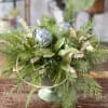 Holiday centerpiece with evergreen foliage, bow, ornaments and seasonal accents.