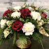 Roses and carnations with winter greens and ribbon tails fill a holiday