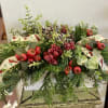 A beautiful arrangement, full of holiday greenery, bright trim, and festive ribbon