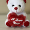 A soft white plush bear with red accents, holding a heart the