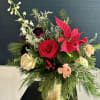 A festive holiday arrangement with winter greens in a gold vase. Medium