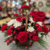 Assorted Christmas greens in a wicker basket filled with red carnations, faux