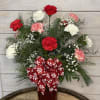 A dozen red, white and peppermint carnations with winter greenery in a