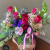 Pink and purple mixed flower arrangement with roses and hydrangea in a glass vase on a wood slice stand.