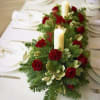 Christmas Dinner table centerpiece. Arrangement of greenery, roses and carnations, and candles.