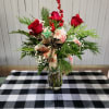 A vase of three red roses accompanied by winter greens and berries.
