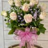 A dozen pink roses arranged in a vase with filler flowers and