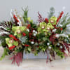 This arrangement features green cymbidium orchids along with seasonal winter greenery. The
