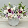 This arrangement combines white and blush flowers with purple toned roses and