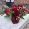 This radiant arrangement features red florals mixed with fragrant pine, and other