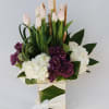 A rectangular vase filled with hydrangeas, purple lilacs, and tulips,  accented