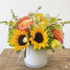 This arrangement include orange free spirit roses, sunflowers, hellebore, hydrangea, daffodils and