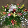 This semi round arrangement of holiday greenery, berries, premium flowers and lilies