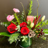 festive greens are collected in a glass container accented with red roses