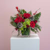 Red roses, winter greens, and holiday accents arranged in a classic glass