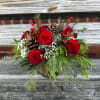 Red roses, white filler and evergreens create the perfect cheery setting. Added
